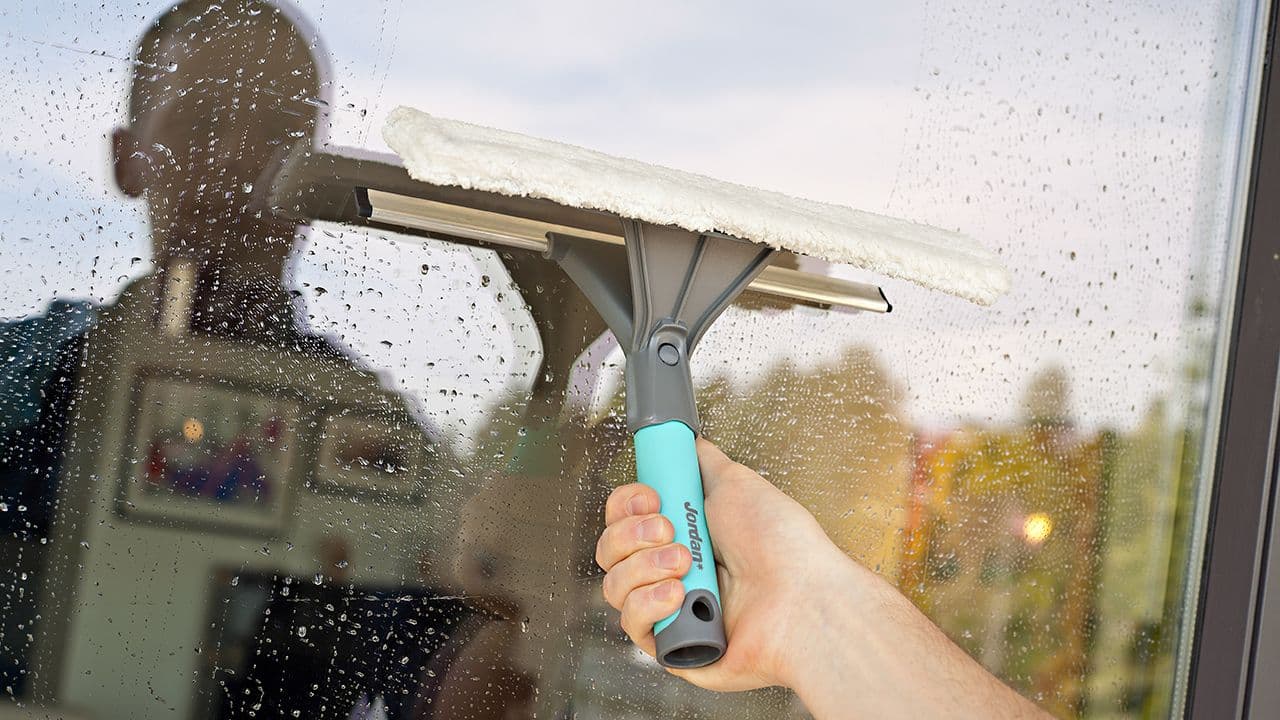 Mann som bruker vindussett for å vaske vinduer ute.