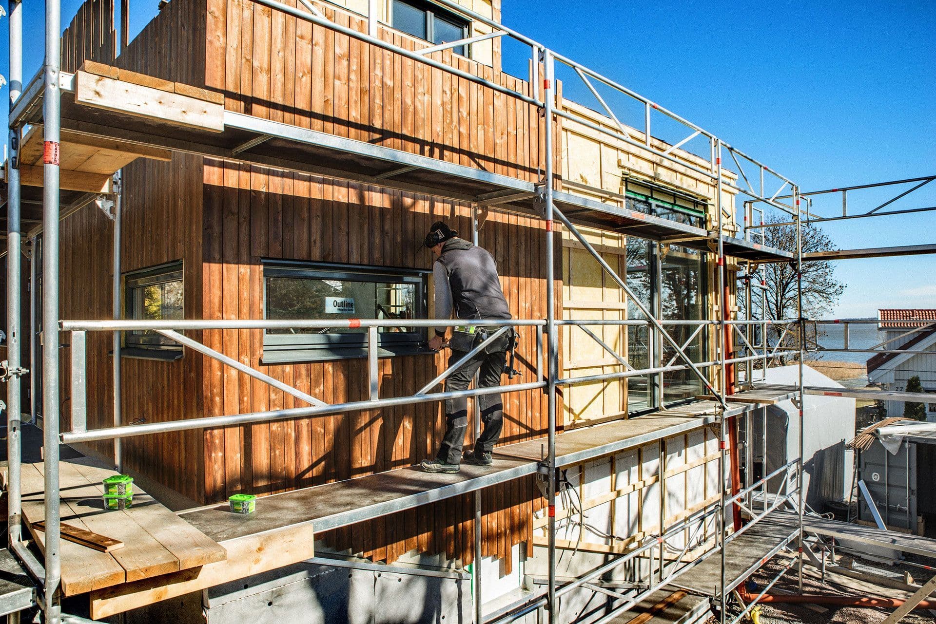 Håndverker i stillas som skrur kledning med fasadeskruer.