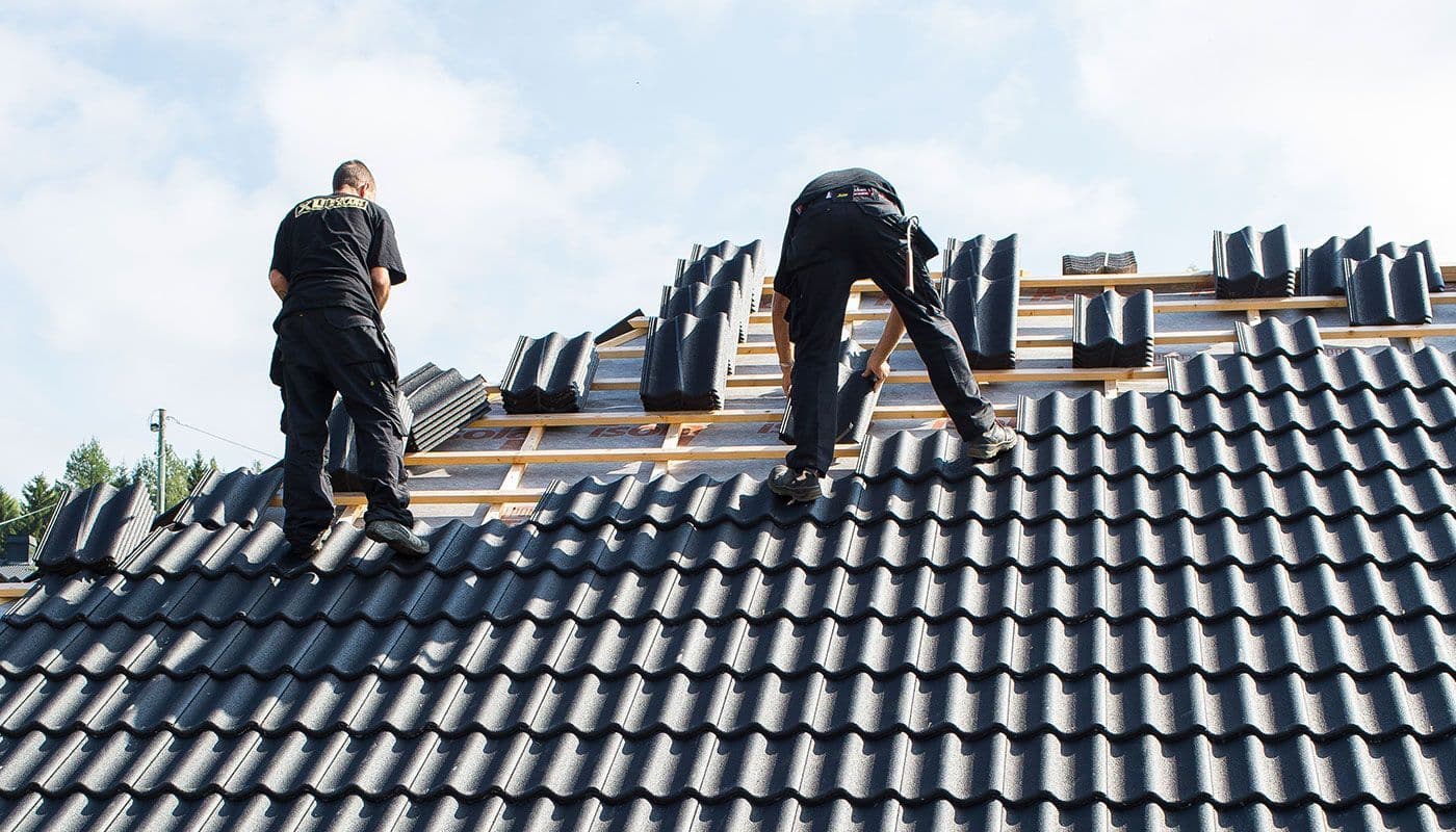 Håndverkere som legger takstein på tak.