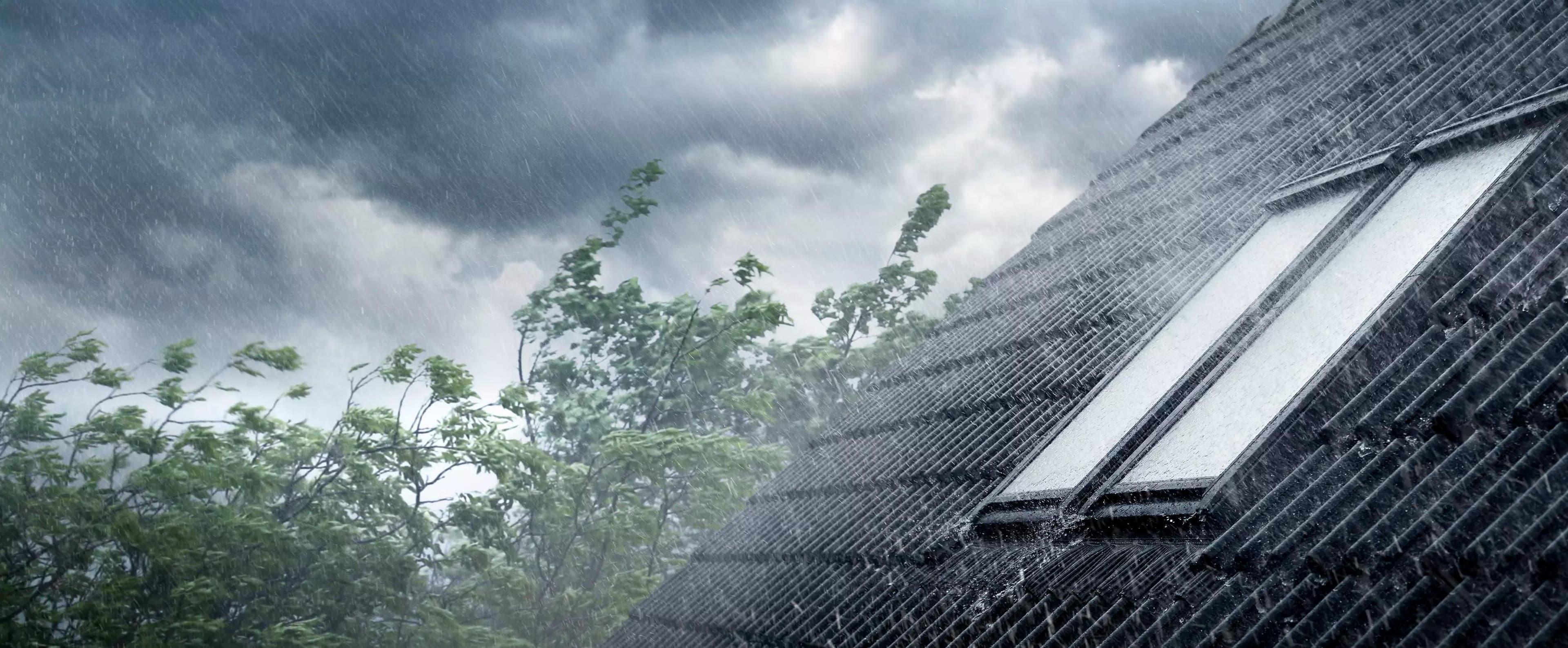 Takvinduer i kraftig regn og vind med mørke skyer i bakgrunnen