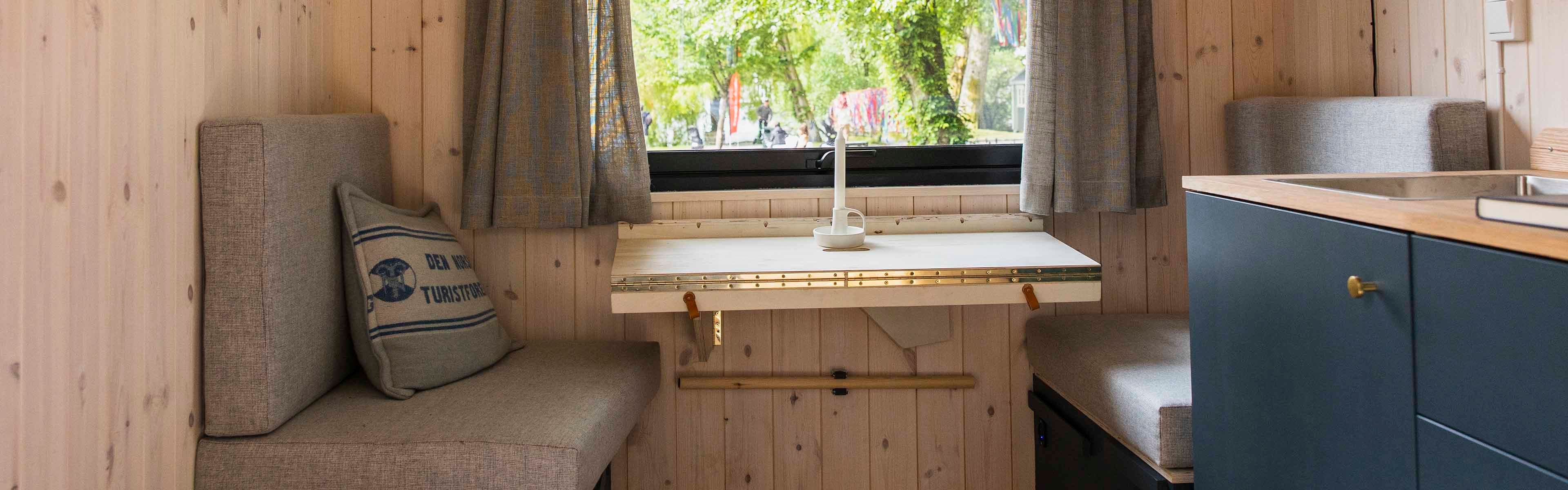 Minihytte med blått kjøkken, sittegruppe med puter og utfellbart bord.