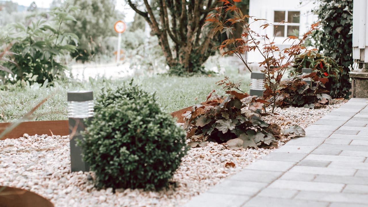 Hage med belegnigsstein, grus, gress og beplantning hvor vann kan renne unna.