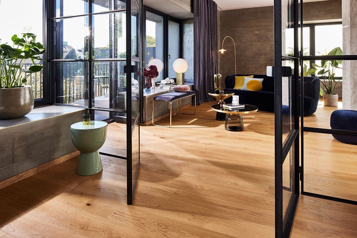 flott stue med glassdører i sort stål og eikeparkett i en varm farge