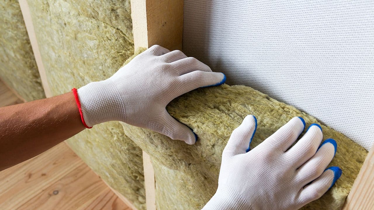 Nærbilde av hender med hansker som putter isolasjon i innvendig vegg.