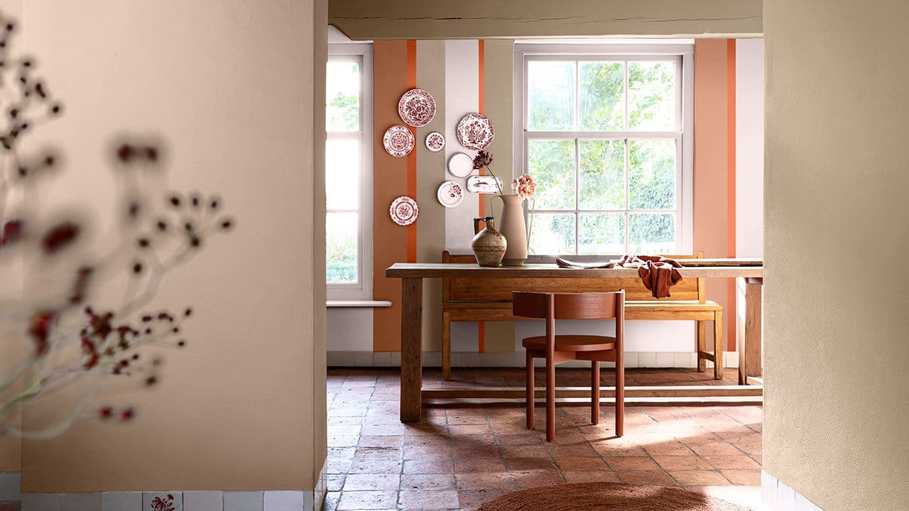 Inngang til spisestue malt i beige, hvitt og ulike oransjetoner med terrakottafliser på gulvet..