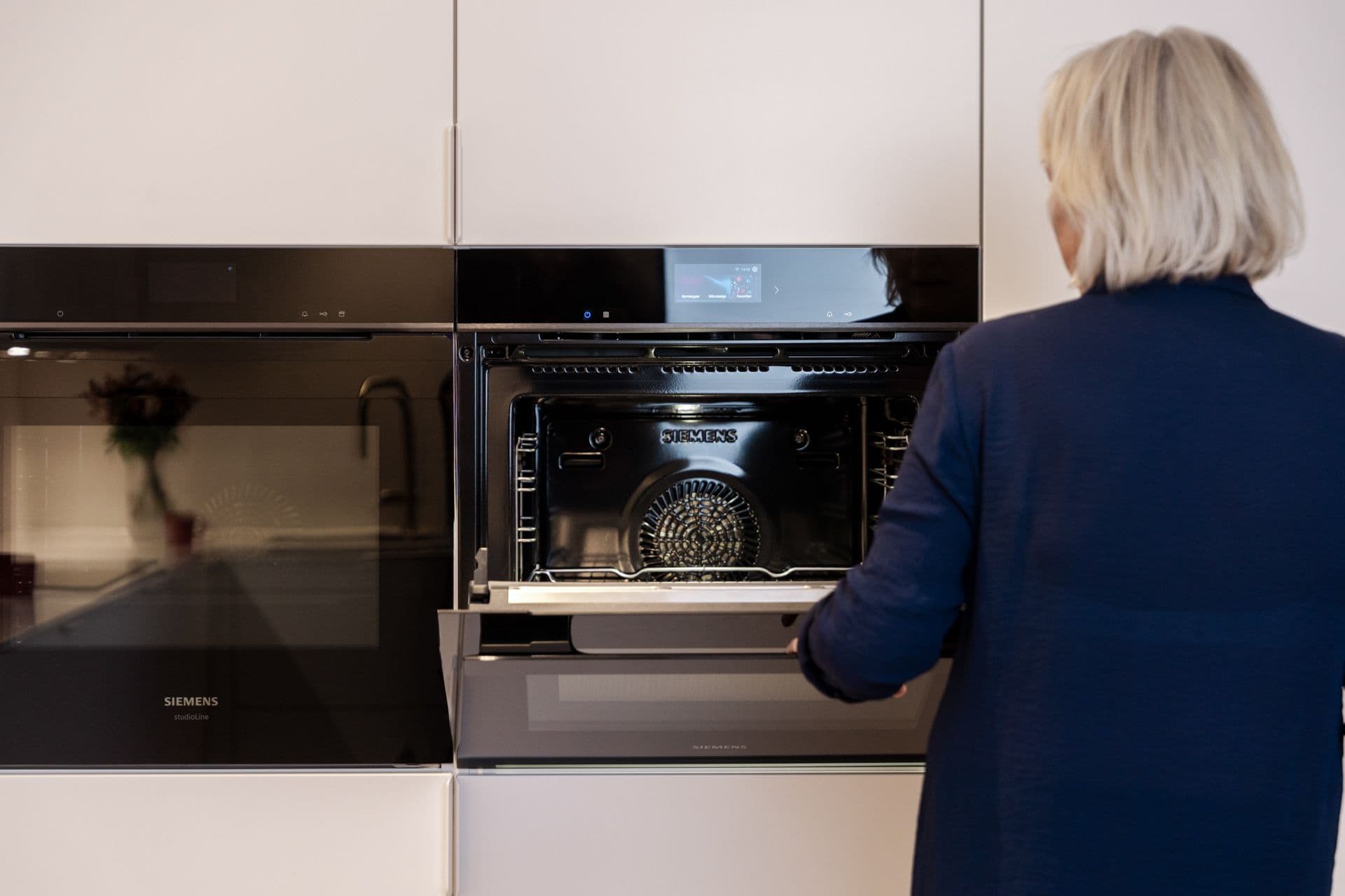 Kvinne som står foran to stekeovner ved siden av hverandre montert i høyskap.