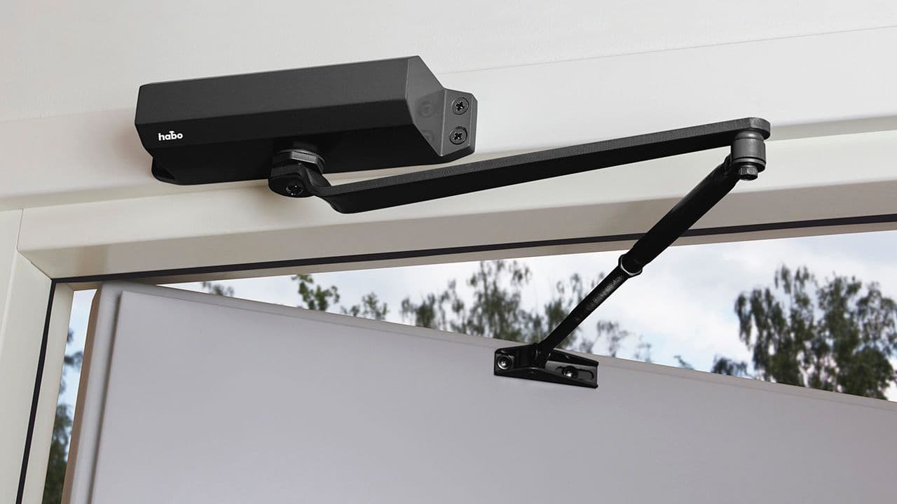 Svart dørlukker med arm på grå ytterdør.