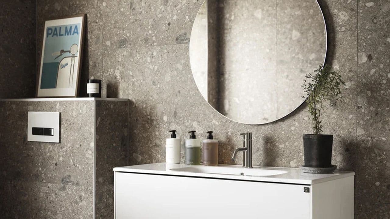 Bad med vegger i naturstein, hvitt baderomsmøbel og rundt speil.