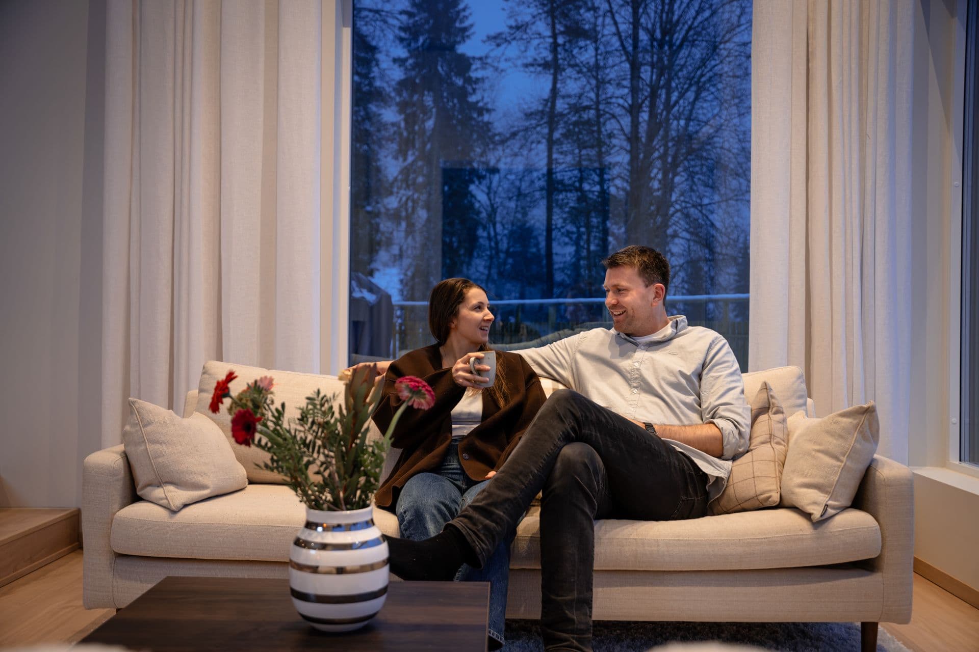 To personer som smiler mot hverandre i en sofa i nytt hus.