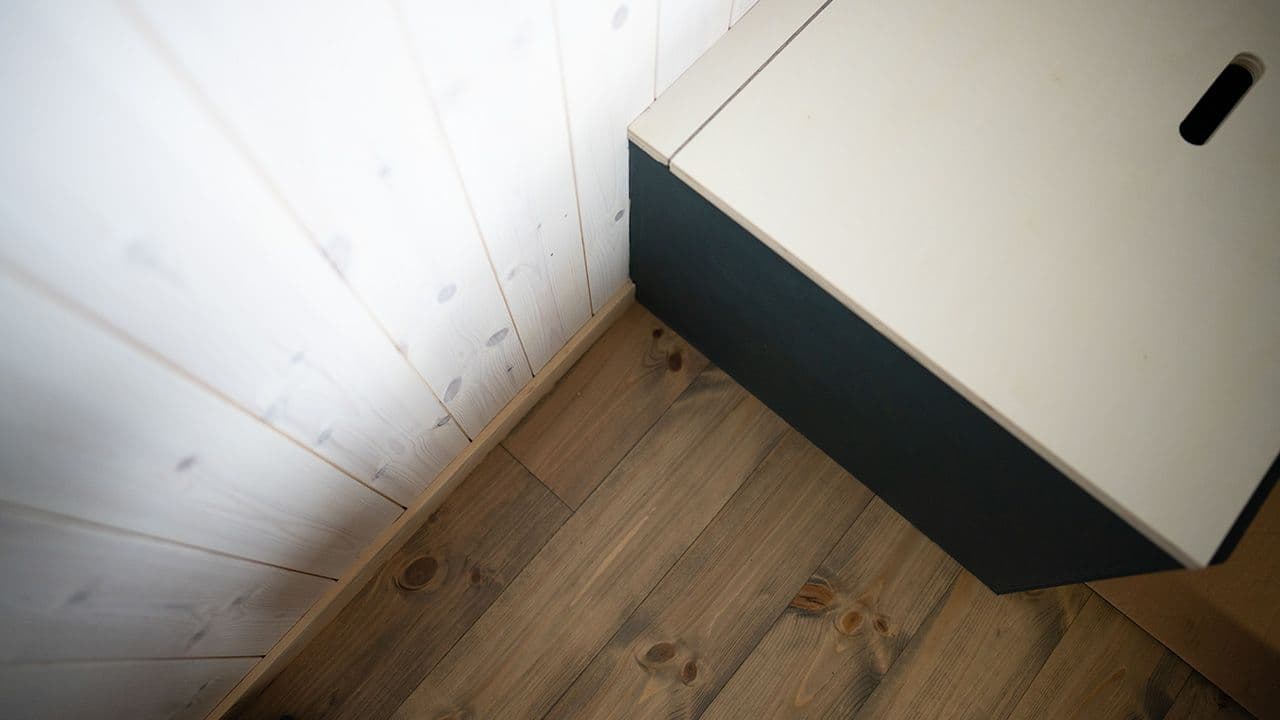 Nærbilde av furupanel, furugulv og oppbevaringskasse.