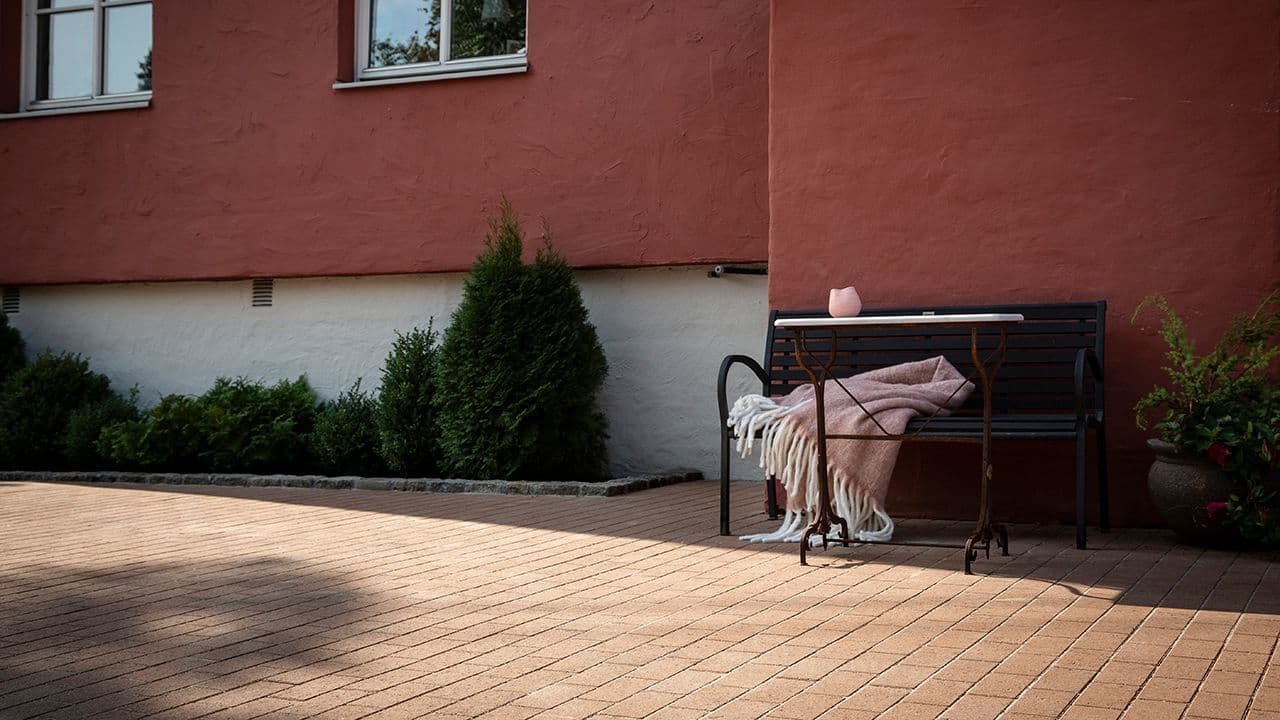 Brun belegningsstein utenfor rødt murhus.